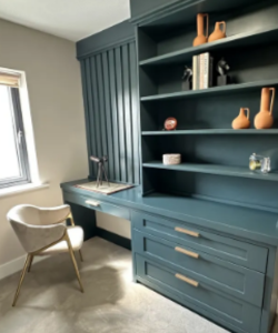 A blue bookcase in a room with a chair and a desk, prepared for an art submission.