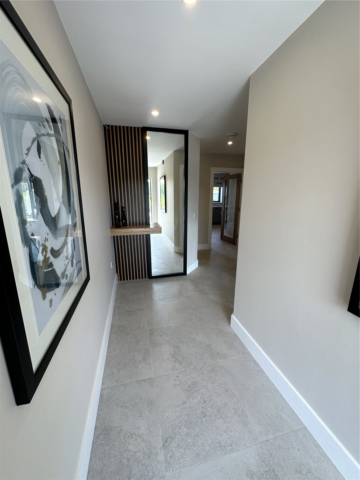 Modern home interior featuring a tiled hallway with framed artwork on the walls, leading to a brightly lit room.