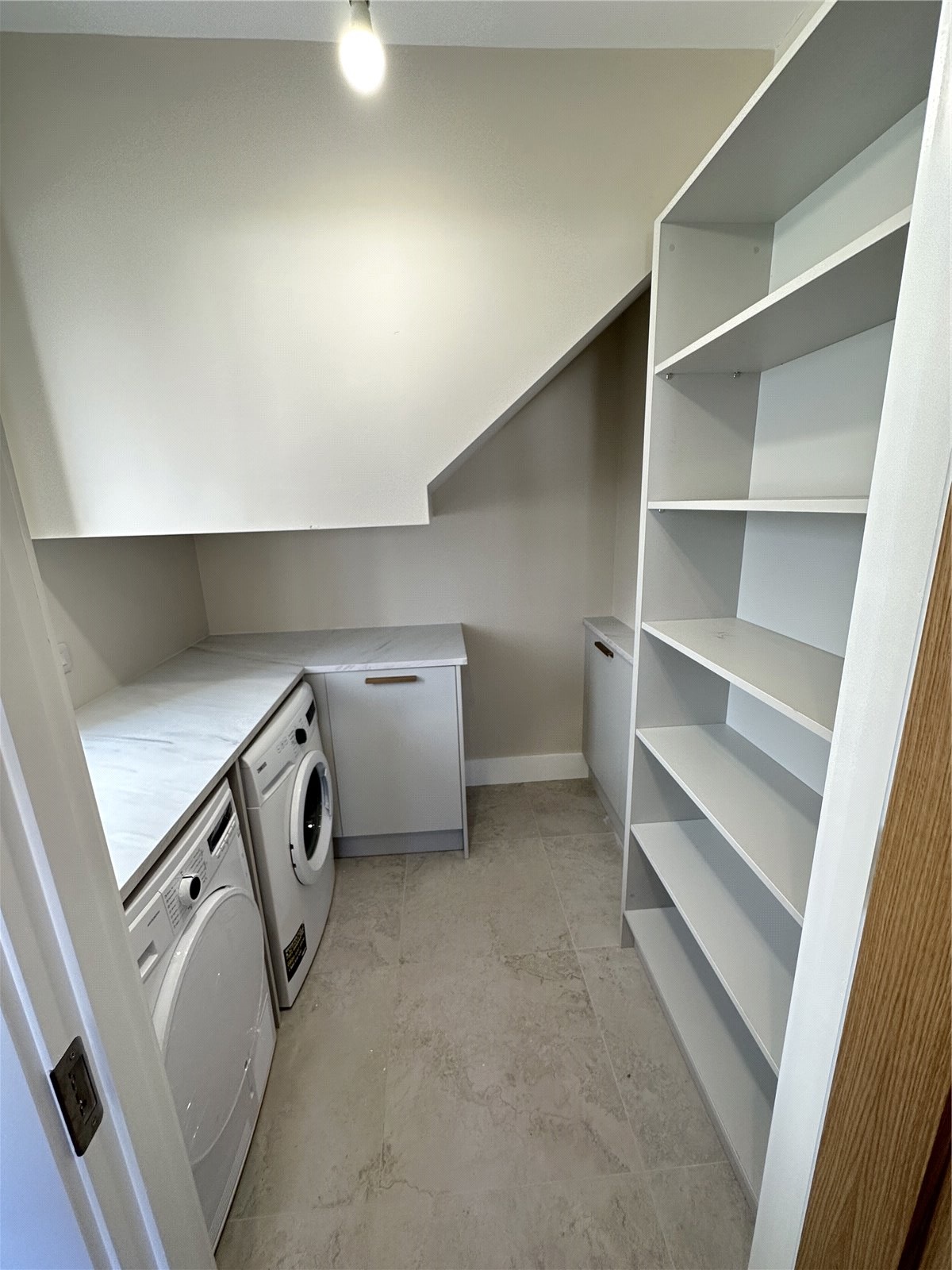 A modern laundry room with white cabinets, built-in shelving, a washer, and a dryer, featuring a neutral color scheme and tiled flooring.